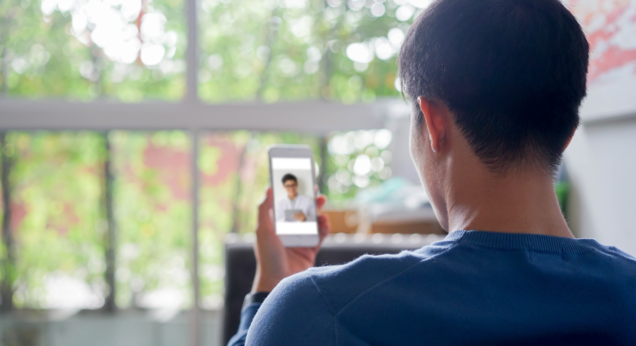 close up rear view of young man using smartphone to video conference to consulting about male hormone and physical with specialist and listen explaining at home for telemedicine health technology life concept