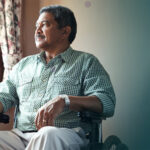 Southeast Asian man in a wheelchair, looking wistfully out a window.