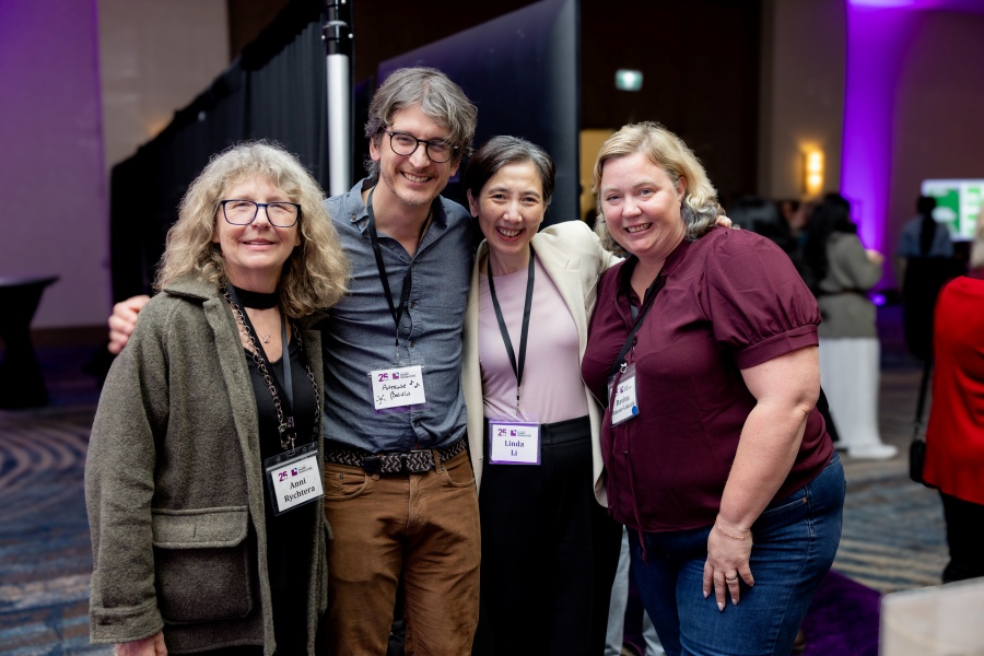 A group of four smiling attendees at the 25th Anniversary event on March 2, 2026, with their hands around each other.