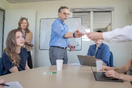 One parent partner shakes hands with another, out of view. They are surrounded by other supportive parents.