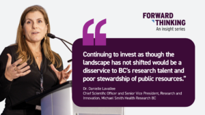 Quote graphic for the Forward Thinking insight series featuring Dr. Danielle Lavallee, Chief Scientific Officer and Senior Vice President, Research and Innovation at Michael Smith Health Research BC. On the left is a photo of Dr. Lavallee speaking at a podium with a microphone, gesturing with her hands during a presentation. On the right, the Forward Thinking logo appears above a quote that reads: ‘Continuing to invest as though the landscape has not shifted would be a disservice to BC’s research talent and poor stewardship of public resources.’ The graphic has a white background with a dark purple quote box and purple quotation marks
